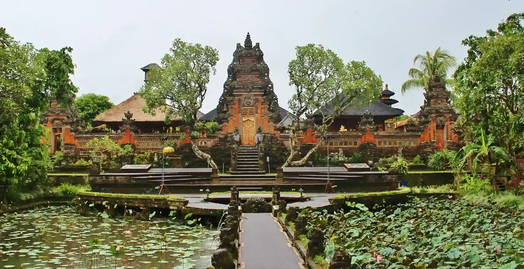 A tiered Balinese palace temple reflected in the still water of its lotus pond
