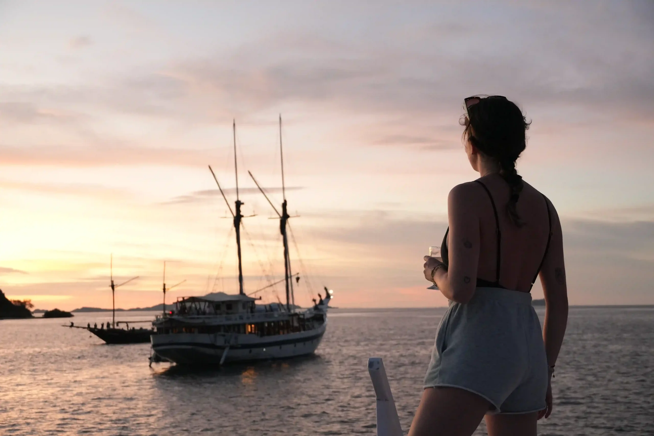 A traveller watching a phinisi lie at anchor off Kalong Island as the sun goes down